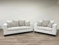 White sofa set with patterned cushions on a wooden floor and light gray walls.